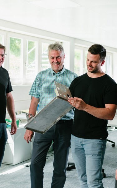 Mehrere Jossi-Mitarbeiter begutachten gemeinsam einen Prototypen und tauschen sich über dessen Konstruktion aus. Die Szene zeigt die enge Zusammenarbeit bei der Entwicklung industrieller Automatisierungslösungen.