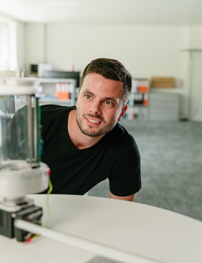 Ein Jossi-Mitarbeiter betrachtet aufmerksam einen technischen Prototypen in den Entwicklungsräumen des Unternehmens. Die Szene vermittelt die Prüfung und Weiterentwicklung einer industriellen Automatisierungslösung.
