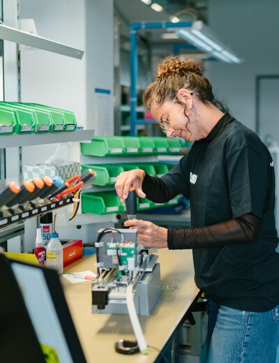 Eine Jossi-Mitarbeiterin montiert und prüft eine Baugruppe an einem modernen Montagearbeitsplatz. Die Szene zeigt präzise Fertigungsarbeit und Qualitätsbewusstsein bei der Herstellung industrieller Automatisierungslösungen.