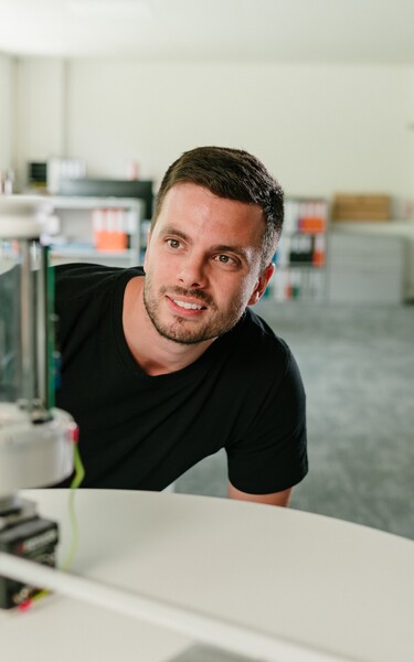 Ein Jossi-Mitarbeiter betrachtet aufmerksam einen technischen Prototypen in den Entwicklungsräumen des Unternehmens. Die Szene vermittelt die Prüfung und Weiterentwicklung einer industriellen Automatisierungslösung.