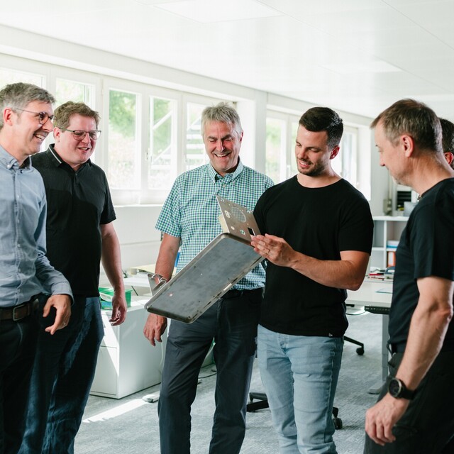 Several Jossi employees examine a prototype together and discuss its design. The scene highlights close collaboration in the development of industrial automation solutions.