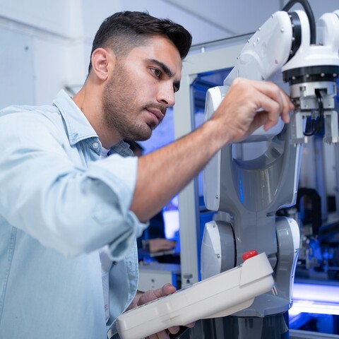 Ein Techniker justiert einen kollaborativen Roboterarm und hält dabei ein Bediengerät in der Hand. Die Szene zeigt die Einrichtung einer automatisierten Produktionsanlage.