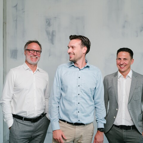 Three Jossi employees stand together, smiling and chatting in a relaxed atmosphere. The image represents trust, mutual respect, and an open company culture.
