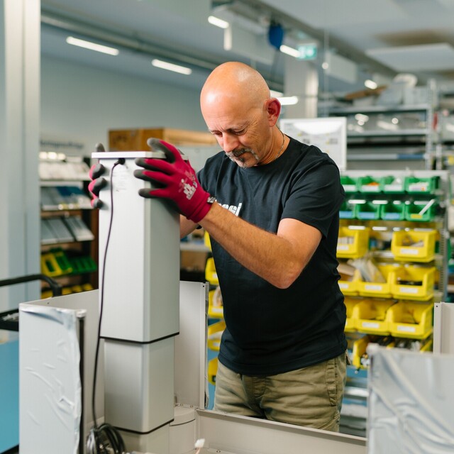 Ein Jossi-Mitarbeiter montiert eine Baugruppe einer industriellen Automatisierungslösung an einem modernen Montagearbeitsplatz. Die Szene zeigt präzise Montagearbeiten und die sorgfältige Fertigung hochwertiger Anlagenkomponenten.