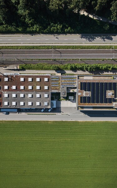 Senkrechte Luftaufnahme des Jossi-Unternehmensstandorts mit Produktions- und Bürogebäuden, Solaranlage auf dem Dach sowie umliegender Verkehrs- und Grünfläche. Die Aufnahme vermittelt einen Überblick über das Firmengelände und die moderne Infrastruktur.
