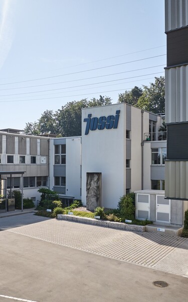 Ansicht des Eingangsbereichs und der Bürogebäude am Jossi-Unternehmensstandort. Die Aufnahme zeigt die moderne Architektur und den Hauptzugang des Unternehmens.