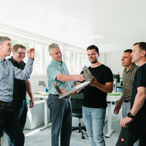 Several Jossi employees discuss a prototype and review its design together. The scene highlights technical collaboration and teamwork in the development of industrial automation solutions.