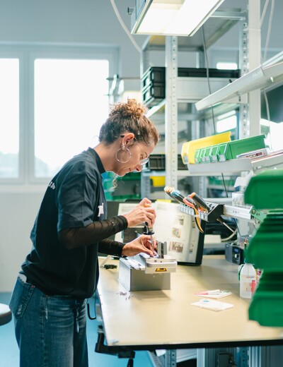 Eine Jossi-Mitarbeiterin montiert eine Baugruppe an einem modernen Montagearbeitsplatz. Die Szene zeigt sorgfältige Handarbeit und präzise Fertigung industrieller Automatisierungslösungen.
