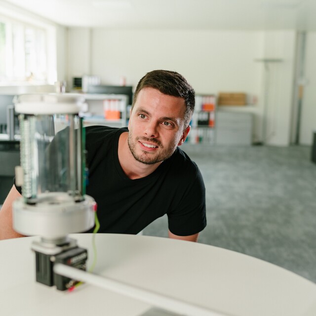 Ein Jossi-Mitarbeiter betrachtet aufmerksam einen technischen Prototypen in den Entwicklungsräumen des Unternehmens. Die Szene vermittelt die Prüfung und Weiterentwicklung einer industriellen Automatisierungslösung.
