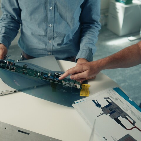 Two Jossi employees inspect an electronic assembly using a technical drawing as reference. The scene highlights the collaborative development and validation of an industrial automation solution.
