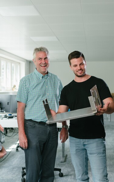 A group of professionals examines a mechanical component together and discusses its design. The scene conveys teamwork, knowledge sharing, and collaboration in an engineering or manufacturing environment.