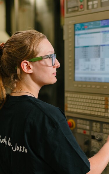 A Jossi employee operates the control panel of a manufacturing machine while monitoring the production process. The scene highlights the precise control and supervision of an industrial automation system.