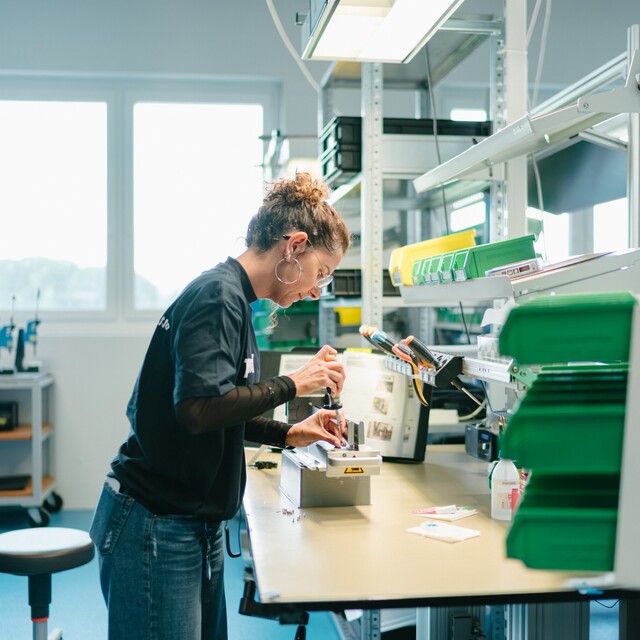Eine Jossi-Mitarbeiterin montiert eine Baugruppe an einem modernen Montagearbeitsplatz. Die Szene zeigt sorgfältige Handarbeit und präzise Fertigung industrieller Automatisierungslösungen.