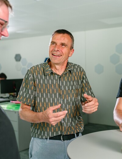 Drei Jossi-Mitarbeiter tauschen sich vor einem technischen Prototypen über dessen Entwicklung und Funktion aus. Die Szene vermittelt Zusammenarbeit, Erfahrungsaustausch und gemeinsame Produktentwicklung im Unternehmen.