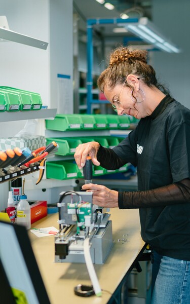 A Jossi employee assembles and inspects a mechanical assembly at a modern workstation. The scene highlights precision manufacturing and quality-focused production of industrial automation solutions.