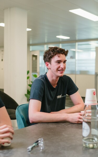 Jossi apprentices sit together around a table, chatting in a relaxed atmosphere. The scene highlights teamwork, young talent development, and an open workplace culture.